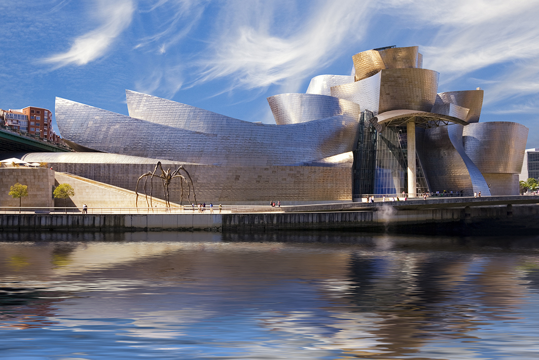 Guggenheim Bilbao museum reflection on the Nervion river, over a cloudy blue sky